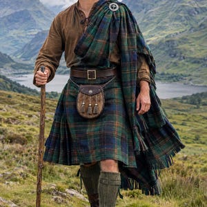Peut inclure: Une chemise marron à manches longues, un kilt à carreaux vert et bleu, et un châle assorti fixé par une broche argentée. Comprend une ceinture en cuir marron, un sporran en fourrure à trois pompons, des chaussettes en laine vert olive et des bottes.