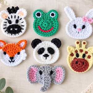 May include: A collection of seven crocheted animal appliques featuring a zebra, frog, rabbit, fox, panda, giraffe, and elephant. Each piece is crafted with yarn in distinct colours including white, black, green, orange, yellow, grey, and pink.