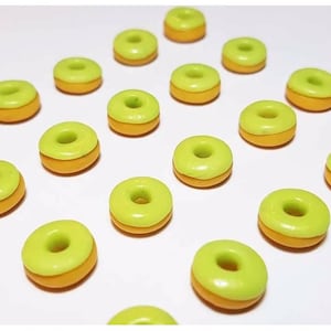 May include: A collection of small, circular donut-shaped charms arranged in a grid pattern. Each piece features a smooth, bright lime green top layer resembling icing, contrasted with a solid, warm orange base layer, creating a two-tone appearance.