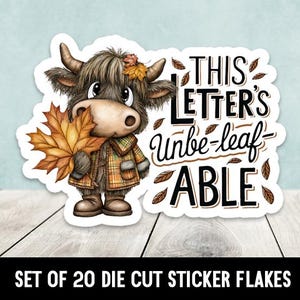 May include: A die-cut sticker featuring a cartoon Highland cow holding a fall leaf. The cow wears a plaid jacket and has a leaf in its hair. Text on the sticker reads "THIS LETTER'S Unbe-leaf-ABLE". The sticker is white with a black border.