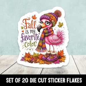 May include: A die-cut sticker featuring a pink flamingo wearing a purple knit hat and a multi-colored striped scarf and boots, standing on autumn leaves. The text reads Fall is my favorite Color, surrounded by small orange and yellow maple leaves.