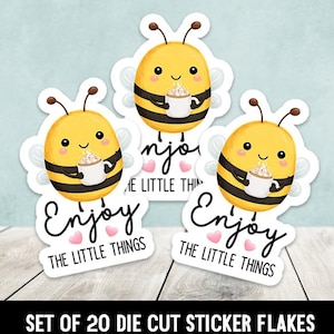May include: A set of die-cut stickers featuring cartoon bees holding coffee mugs. The yellow and black bees have smiling faces and are surrounded by white cloud-shaped outlines. The stickers have the text "Enjoy the little things".