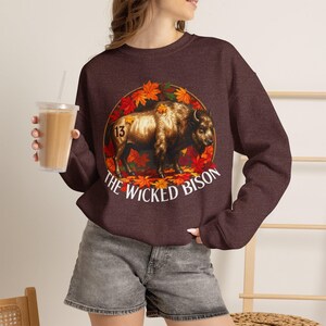 May include: A dark maroon crewneck sweatshirt featuring a graphic of a brown bison standing amidst vibrant orange and red autumn leaves inside a circular frame. The number 13 is on the bison's flank, and the text THE WICKED BISON is below.