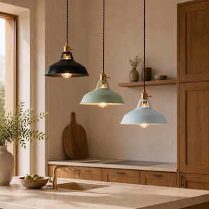May include: Three pendant lights hanging in a row, featuring dome-shaped metal shades in black, sage green, and light blue. Each lamp has a brass-toned fixture at the top, a visible light bulb, and a twisted dark cord suspended from the ceiling.
