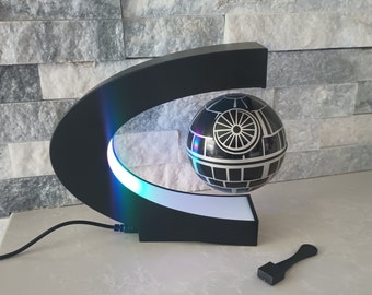 May include: A black magnetic levitating stand with a white light ring and a black and silver Death Star model floating above it. The stand has a black cord.