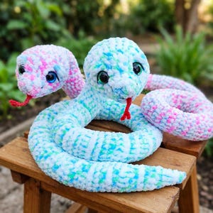 Puede incluir: Un juguete de serpiente de peluche de dos cabezas hecho de hilo suave y jaspeado en tonos blanco, azul claro y rosa. Cada cabeza presenta grandes ojos de seguridad negros brillantes y una pequeña lengua de hilo rojo brillante.