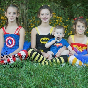 May include: Four children wearing superhero-themed costumes with tulle skirts and patterned leggings. The costumes feature Captain America, Batman, Superman, and Wonder Woman emblems. The text Pampered Paisley is overlaid on the image.