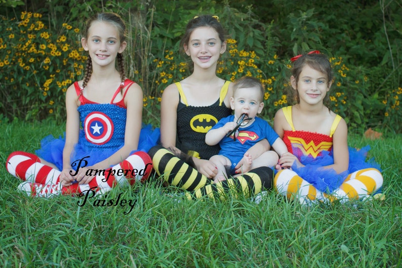 May include: Four children wearing superhero-themed costumes with tulle skirts and patterned leggings. The costumes feature Captain America, Batman, Superman, and Wonder Woman emblems. The text Pampered Paisley is overlaid on the image.