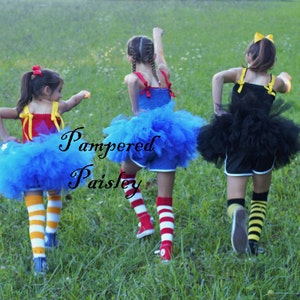 May include: Three outfits featuring tulle skirts and tank tops with shoulder ties. One outfit is red and blue with yellow and white striped socks. Another is blue with red and white striped socks. The third is black with yellow and black striped socks.