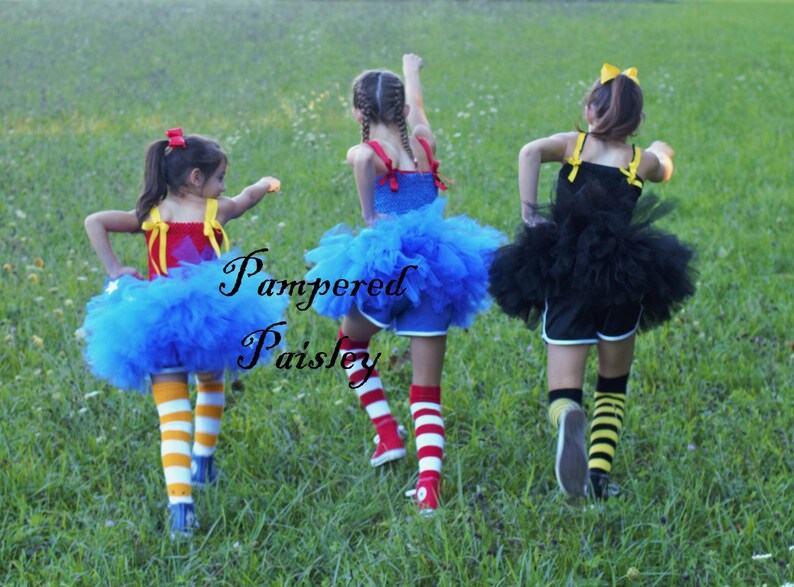 May include: Three outfits featuring tulle skirts and tank tops with shoulder ties. One outfit is red and blue with yellow and white striped socks. Another is blue with red and white striped socks. The third is black with yellow and black striped socks.