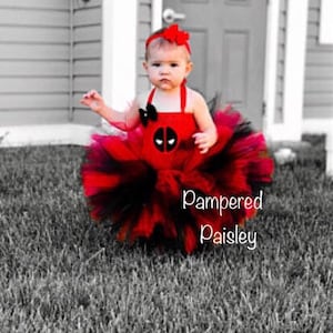 K&ouml;nnte beinhalten: Ein rot-schwarzes Tutu-Kleid mit einem Deadpool-Charakter-Emblem auf dem Oberteil, einem passenden roten Stirnband mit Schleife und einem mehrlagigen T&uuml;llrock. Der Text Pampered Paisley ist unten rechts im Bild zu sehen.