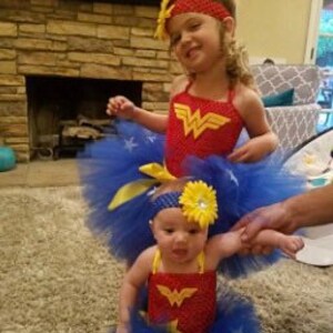 May include: Two matching Wonder Woman themed outfits consisting of red crochet tops with yellow W logos, blue tulle skirts with white star accents, and coordinating headbands featuring yellow flowers, designed for two different sized individuals.