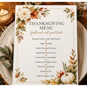 May include: A rectangular Thanksgiving menu card featuring a white background with a gold border, decorated with watercolour illustrations of autumn leaves, a white dahlia, and a white pumpkin. The text reads Thanksgiving Menu, Gathered with gratitude, and lists various holiday food items.