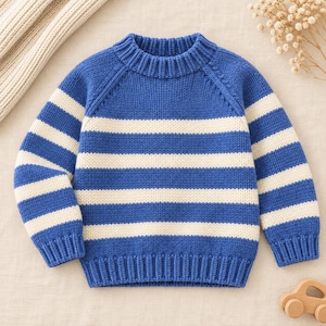 May include: A long-sleeve knit sweater featuring horizontal stripes in royal blue and cream. The garment has a ribbed crew neckline, ribbed cuffs, and a ribbed hem, with raglan sleeves and a thick, textured yarn construction throughout the piece.