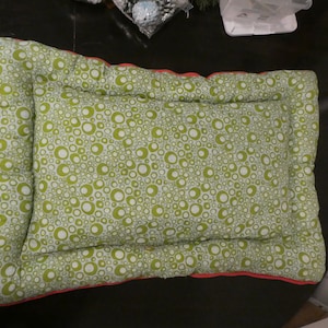 May include: A green and white pet bed with a circle pattern. The bed has a red border.