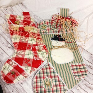 May include: Two handmade Christmas stockings, one red and white plaid with holly and bells, the other green and white striped with a snowman applique. Both stockings have a patchwork design and are decorated with frayed edges and buttons.