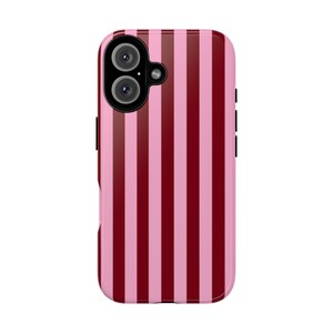 Puede incluir: Una funda rectangular para smartphone con un patrón de rayas verticales en tonos alternos de rojo burdeos oscuro y rosa pastel claro. La funda incluye un recorte negro para el módulo de cámara en la esquina superior izquierda.