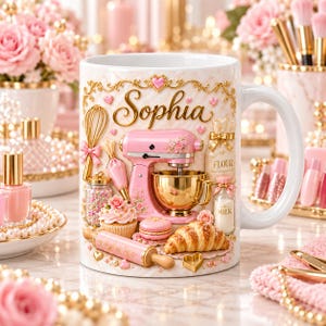 May include: A white ceramic mug featuring the name Sophia in gold script, decorated with a pink stand mixer, a gold mixing bowl, a whisk, a rolling pin, a cupcake, a croissant, a macaron, a jar of sprinkles, and a bottle labeled milk.