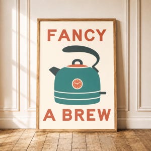 Puede incluir: Una lámina enmarcada sobre fondo crema que muestra una tetera de color verde azulado con un asa gris oscuro y un pequeño reloj en el lateral. El texto FANCY aparece en naranja encima y el texto A BREW aparece en naranja debajo.
