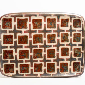 May include: A rectangular ceramic tray featuring a repeating grid pattern of dark brown cross shapes and recessed squares filled with a mottled glaze of deep red, burnt orange, and hints of teal, all set against a cream-colored background.