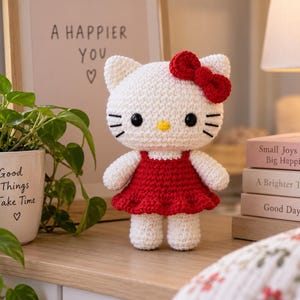 Peut inclure: Une poupée chat crochetée blanche avec des yeux noirs, un nez jaune et des moustaches noires, portant une robe rouge et un nœud rouge assorti sur la tête. La poupée a une tête arrondie et un petit corps avec des bras et des jambes courts.