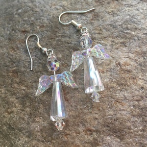 May include: A pair of silver dangle earrings featuring crystal angel charms. The angels have iridescent wings and clear bodies.