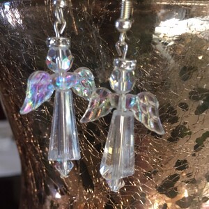 May include: A pair of silver angel-shaped earrings with iridescent crystal beads. The earrings are hanging from silver hooks.