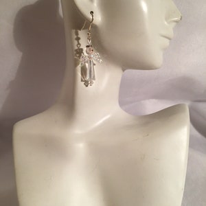 May include: Crystal angel dangle earrings with a gold-tone hook. The earrings are on a white mannequin.