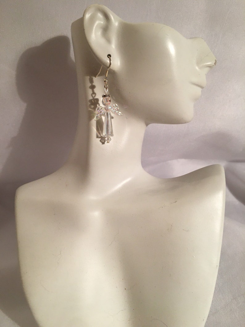 May include: Crystal angel dangle earrings with a gold-tone hook. The earrings are on a white mannequin.