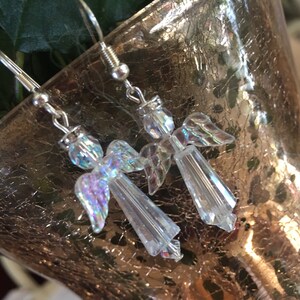 May include: A pair of silver dangle earrings featuring iridescent angel charms. The angels are made of clear crystal with iridescent wings.