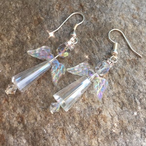 May include: A pair of silver dangle earrings featuring iridescent crystal angel wings. The wings are made of faceted glass beads and are attached to a silver hook.