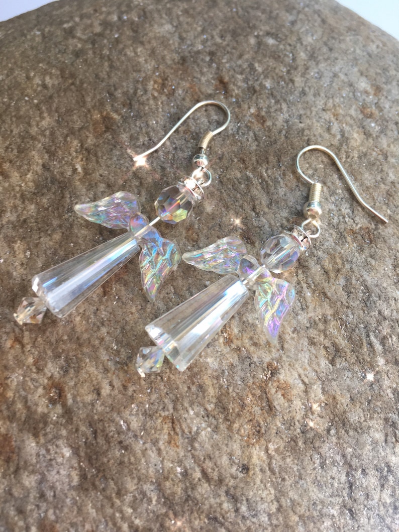 May include: A pair of silver dangle earrings featuring iridescent crystal angel wings. The wings are made of faceted glass beads and are attached to a silver hook.