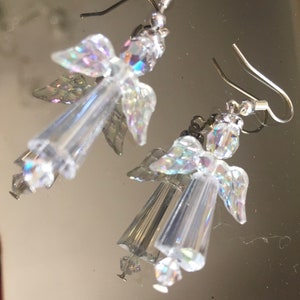 May include: A pair of silver dangle earrings featuring iridescent angel wings and clear crystal beads.