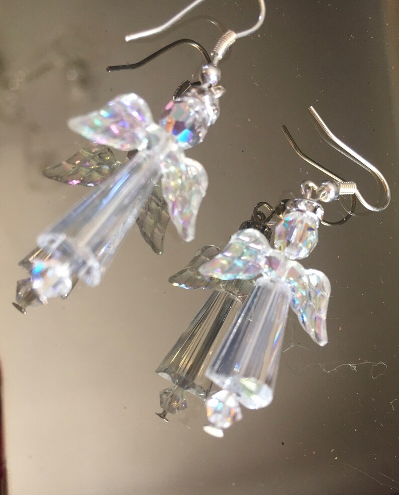 May include: A pair of silver dangle earrings featuring iridescent angel wings and clear crystal beads.