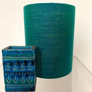 May include: A teal blue lampshade with a textured fabric finish sits next to a teal blue ceramic planter with a geometric pattern.