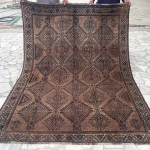 May include: A large rectangular area rug featuring a dark brown and black color palette. The rug displays a repeating geometric diamond pattern across the center field, framed by a wide, intricate border with detailed tribal-inspired motifs.