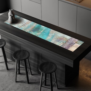 May include: A dark wood kitchen island with a rectangular, abstract art design in shades of blue, teal, and purple. Two neutral-toned vases sit on the island. Three black stools are positioned in front of the island.
