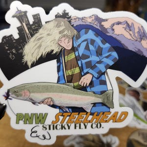 May include: A sticker featuring a cartoon illustration of a person holding a steelhead trout. The background features a cityscape with a mountain range. The sticker has the text "PNW STEELHEAD & STICKY FLY CO."