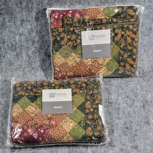 Può includere: Due federe confezionate con un design patchwork e motivi floreali in tonalità verde scuro, bordeaux e beige. Ogni articolo avvolto nella plastica include un'etichetta bianca con il testo Home Collection e la parola sham stampata sotto.