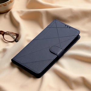 May include: A dark blue rectangular phone case with a magnetic closure flap and a geometric pattern of intersecting lines across the front surface. The lower section features a textured finish, while the upper portion remains smooth and matte.