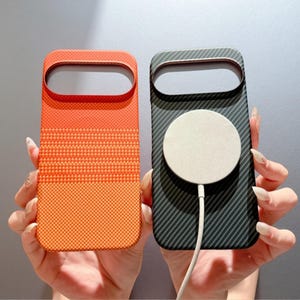 Op de afbeelding: Twee rechthoekige telefoonhoesjes met een grote horizontale camera-uitsparing aan de bovenkant. Het linker hoesje heeft een feloranje verloop met een fijn stippenpatroon. Het rechter hoesje is zwart met een koolstofvezeltextuur en een ronde magnetische oplader.
