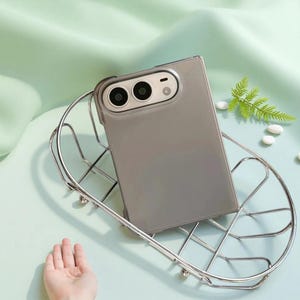 Peut inclure: Une coque de smartphone rectangulaire avec une finition gris mat translucide et une découpe d'appareil photo proéminente comportant trois ouvertures circulaires, reposant dans un panier en fil métallique argenté.