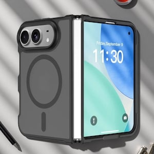Puede incluir: Una funda negra para smartphone plegable con acabado mate, que presenta un anillo de carga magnético circular en la parte posterior, un módulo de cámara elevado con dos lentes y una pantalla que muestra el viernes 9 de septiembre y las 11:30.