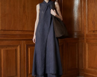 May include: A sleeveless, floor-length dark gray wrap dress with a high neckline and a matching pair of wide-leg trousers. A large, dark brown shoulder bag is carried on one side, and the outfit is completed with pointed-toe brown shoes.