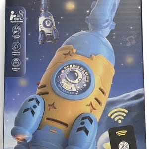 May include: A space-themed bubble machine in the shape of a rocket, coloured blue and yellow, featuring a circular astronaut graphic. The packaging displays the text "SPACE THEME BUBBLE MACHINE" and includes a black remote control with a power icon.