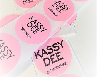 May include: Multiple pink round stickers with the text "Kassy Dee @TSWCOUTURE" in black lettering.