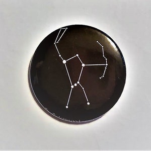 May include: A black button with a white outline of the constellation Cassiopeia.