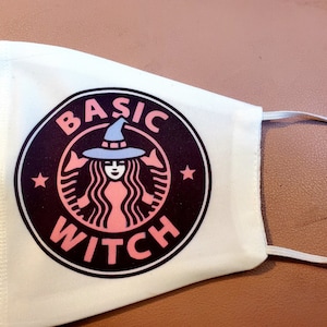 May include: White face mask with a black and white logo that says "BASIC WITCH" with a pink witch silhouette inside the logo.