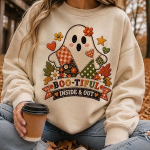 Peut inclure: Un sweat-shirt beige à col rond orné d'un motif central représentant un fantôme composé de divers tissus à motifs, entouré de fleurs, de cœurs et d'étoiles colorés. Sous le fantôme, une bannière affiche le texte BOO-TIFUL INSIDE & OUT.
