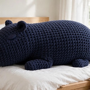 Peut inclure: Un grand coussin en peluche bleu marine foncé en forme d'hippopotame. Le coussin est fabriqué à partir d'un fil tricoté épais et texturé, avec un corps arrondi, des pattes courtes, de petites oreilles et des yeux fermés brodés sur le côté.